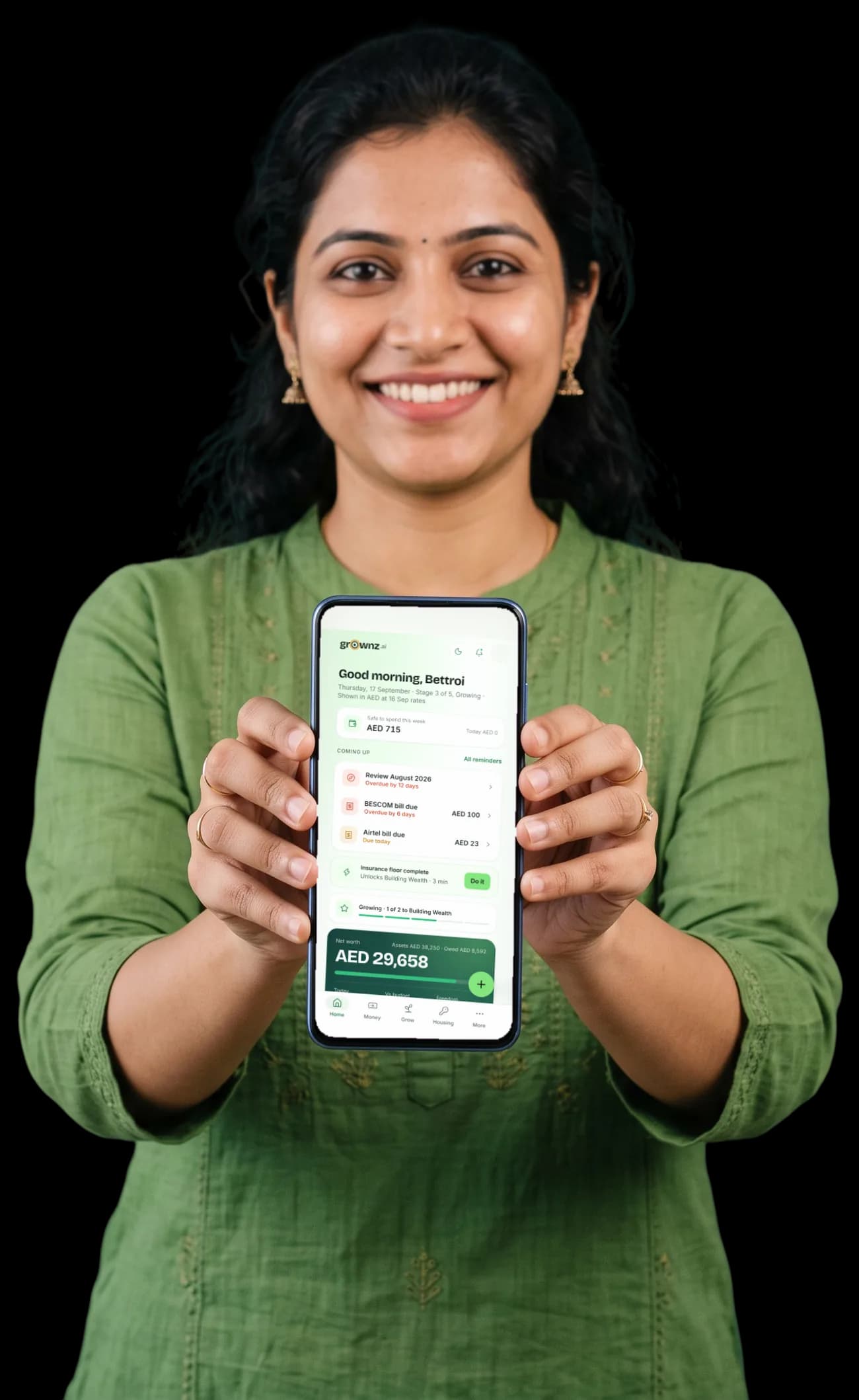 A woman in a green kurta holding her phone up to the camera, the Grownz home screen showing