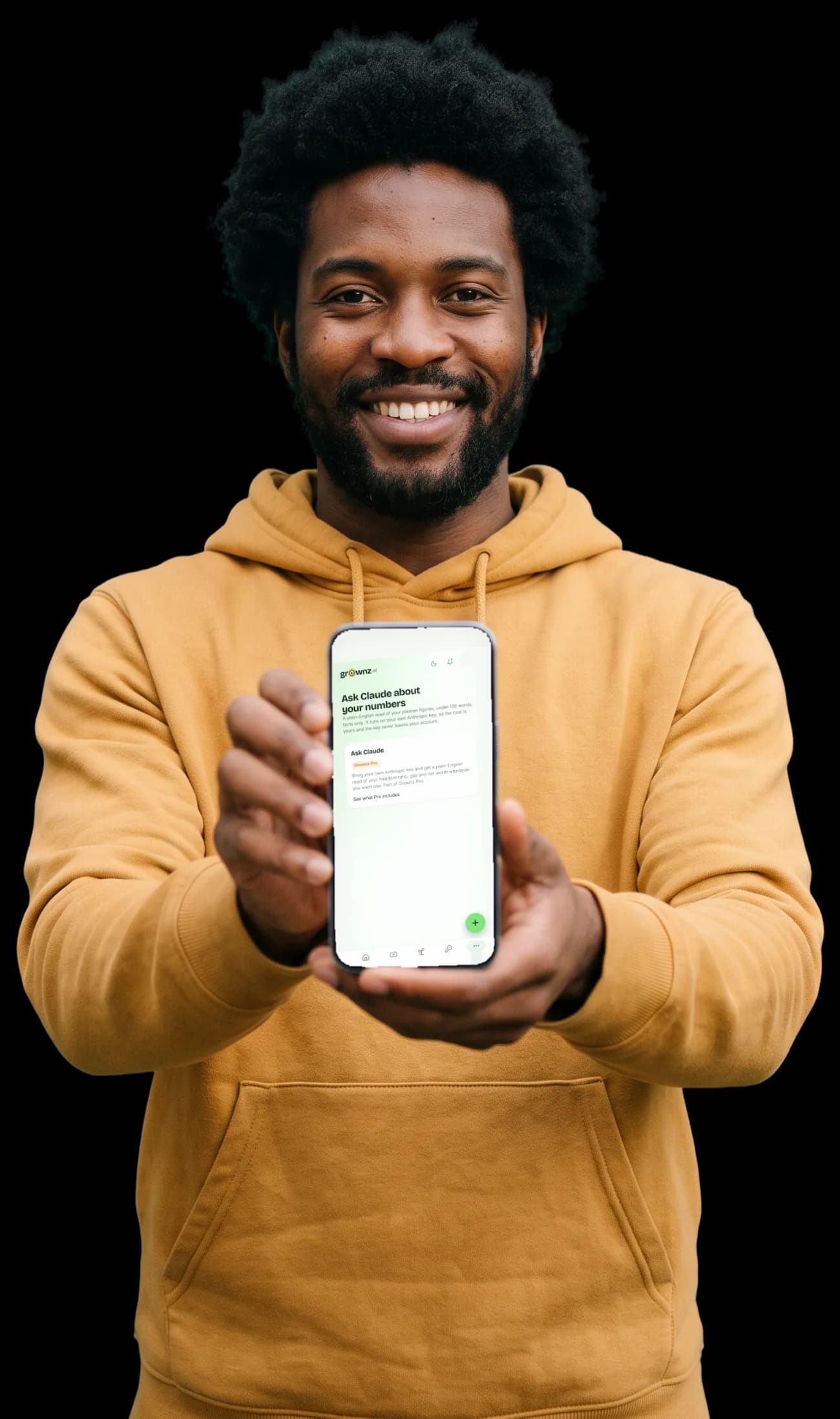A man in a mustard hoodie grinning and holding his phone up to the camera, the assistant screen showing