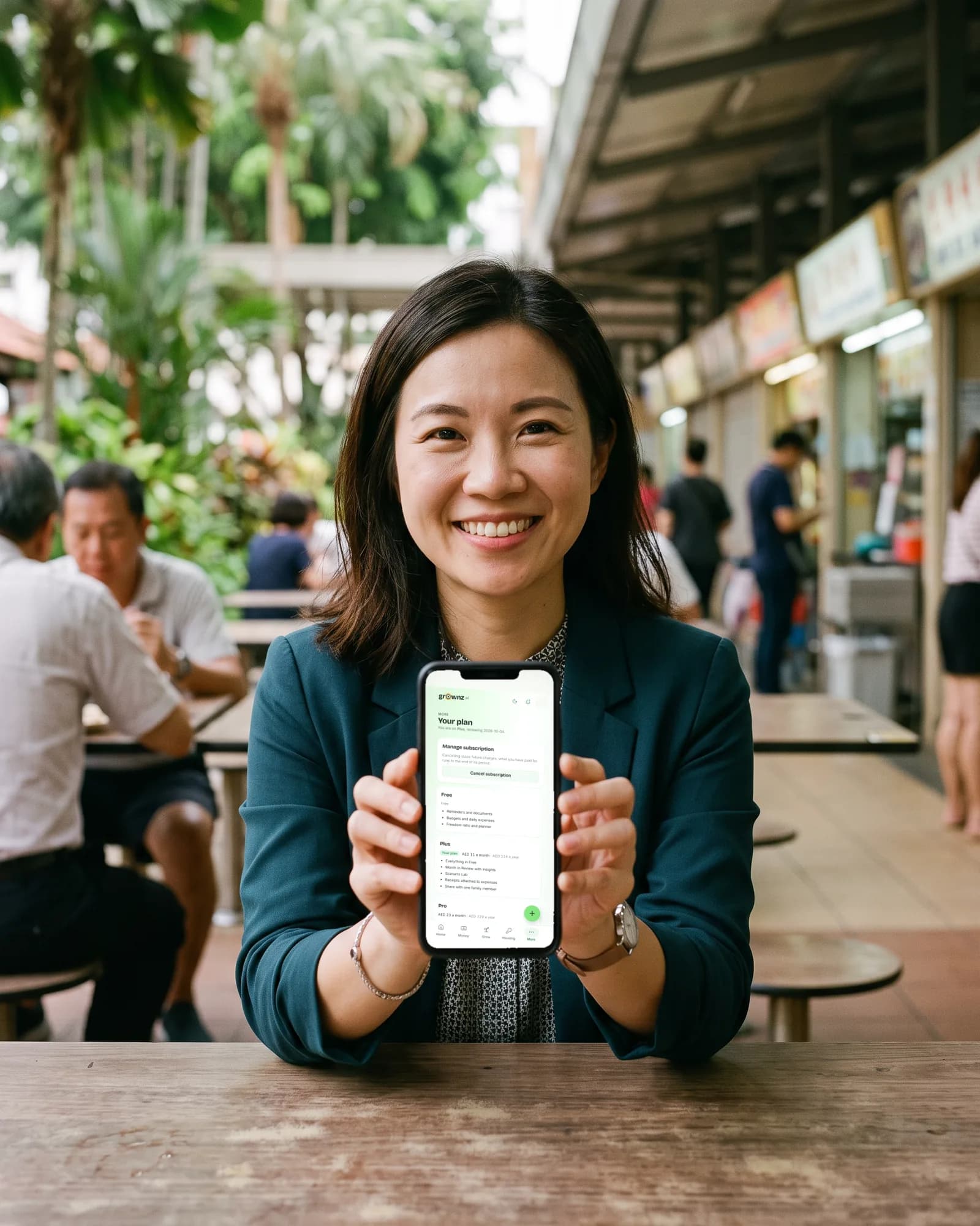 A woman in office wear at a hawker centre holding her phone up to the camera, the Your plan screen showing