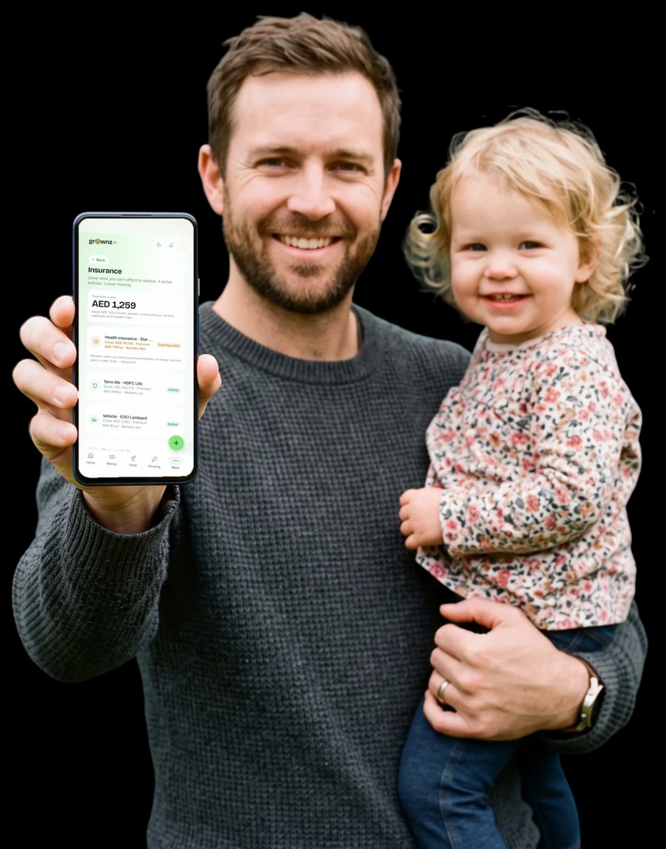 A father with a toddler on his hip holding a phone up to the camera, the Insurance screen showing