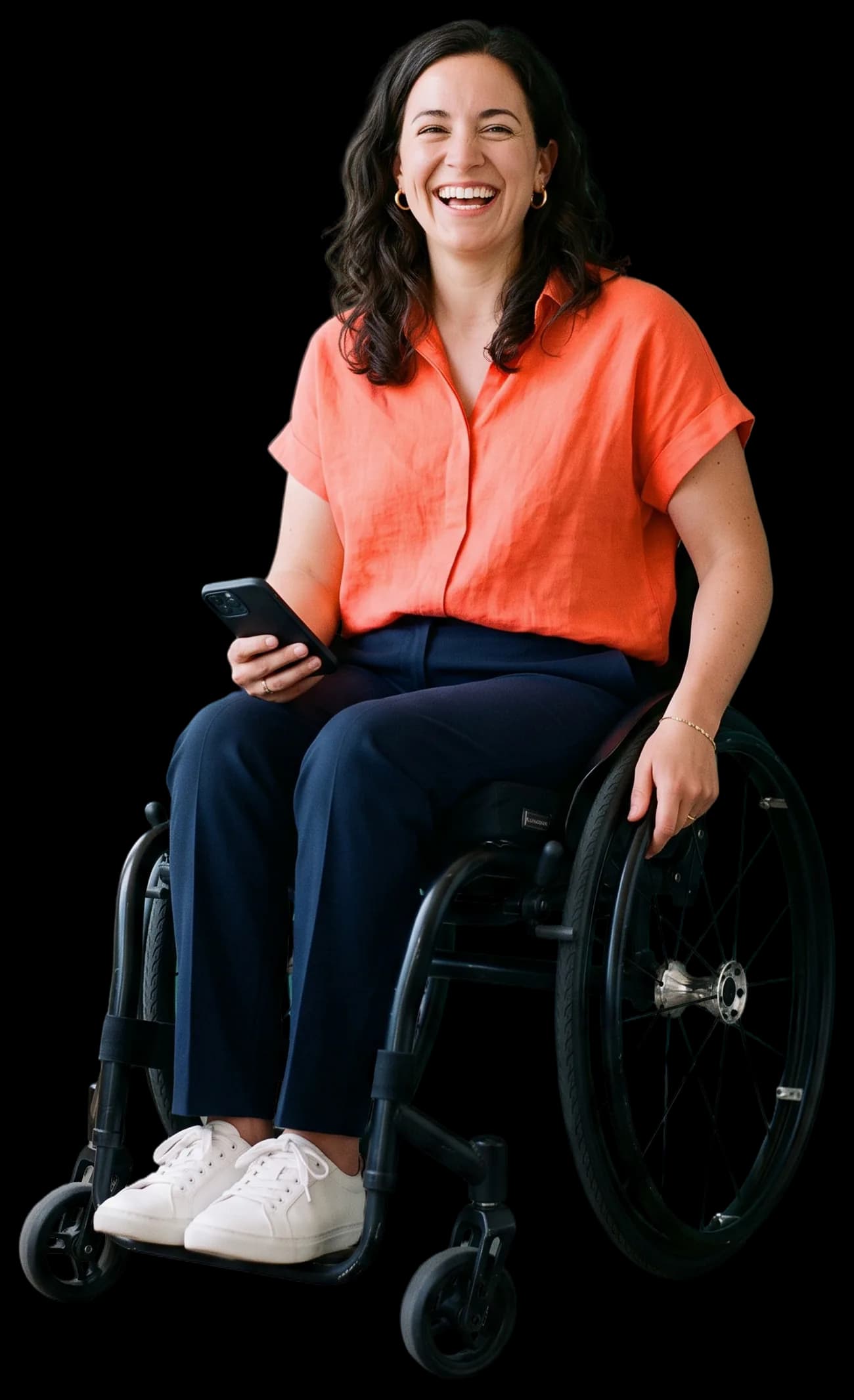 A woman in a wheelchair laughing at the camera, phone in hand