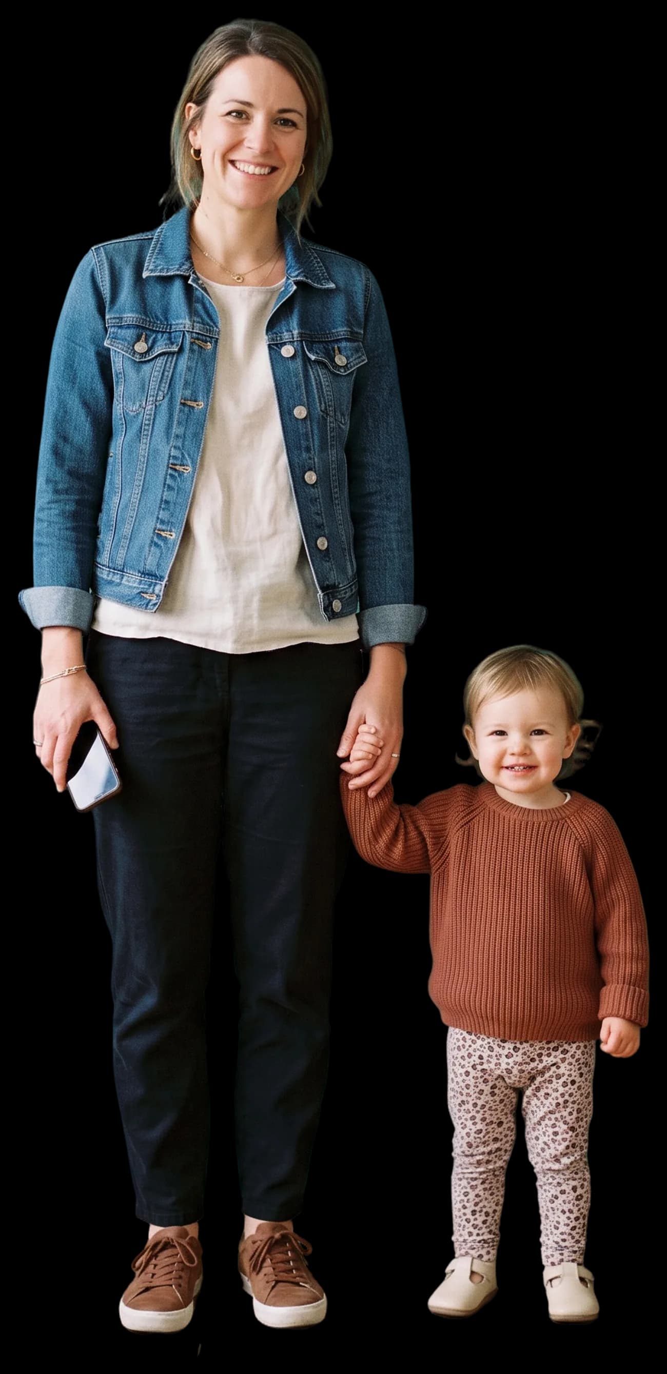 A mother holding a toddler by the hand, smiling at the camera