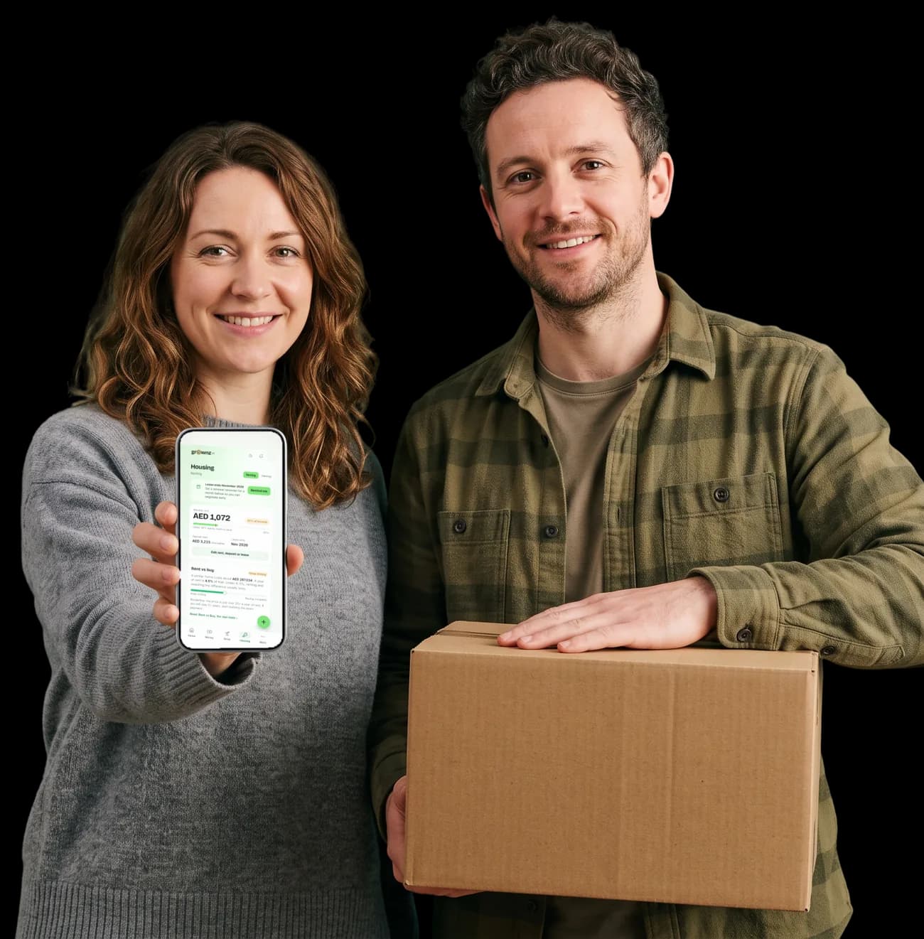 A couple beside a moving box holding a phone up to the camera, the Housing screen showing