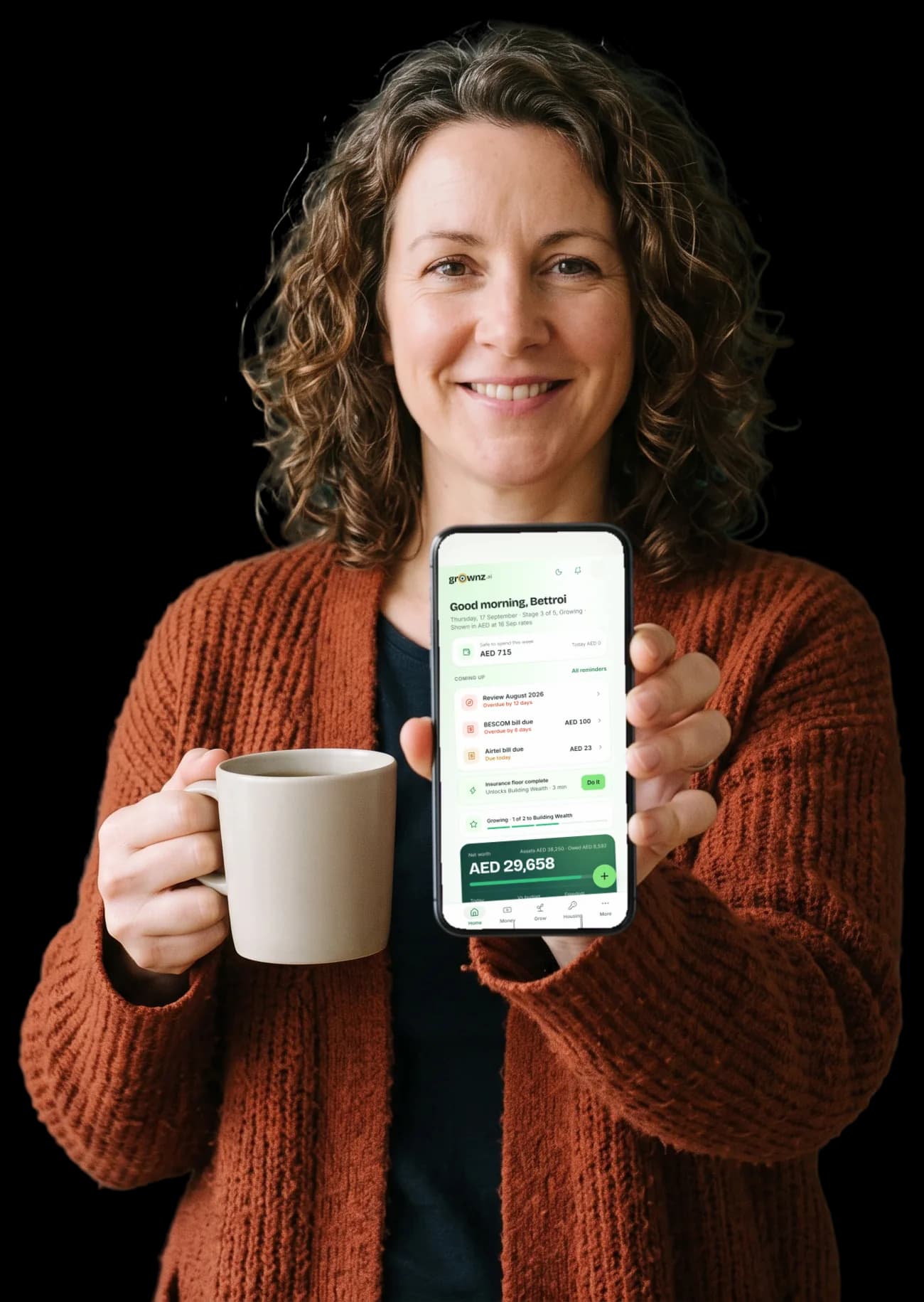 A woman with a mug of tea holding her phone up to the camera, the Grownz home screen showing