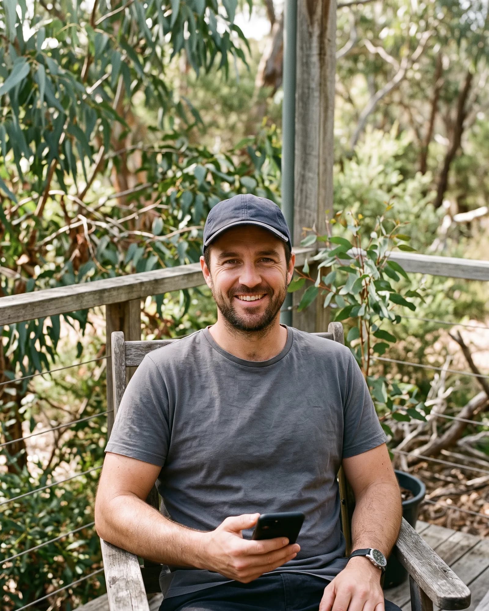A man in a cap on a verandah smiling at the camera